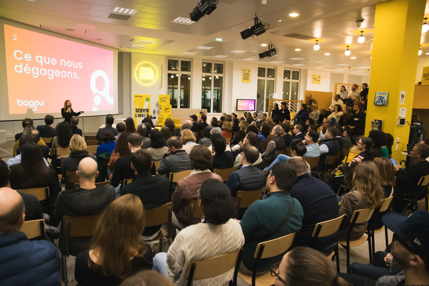 Une conférence Bagou&nbsp;: la personne qui anime devant sa diapositive, face à une salle comble